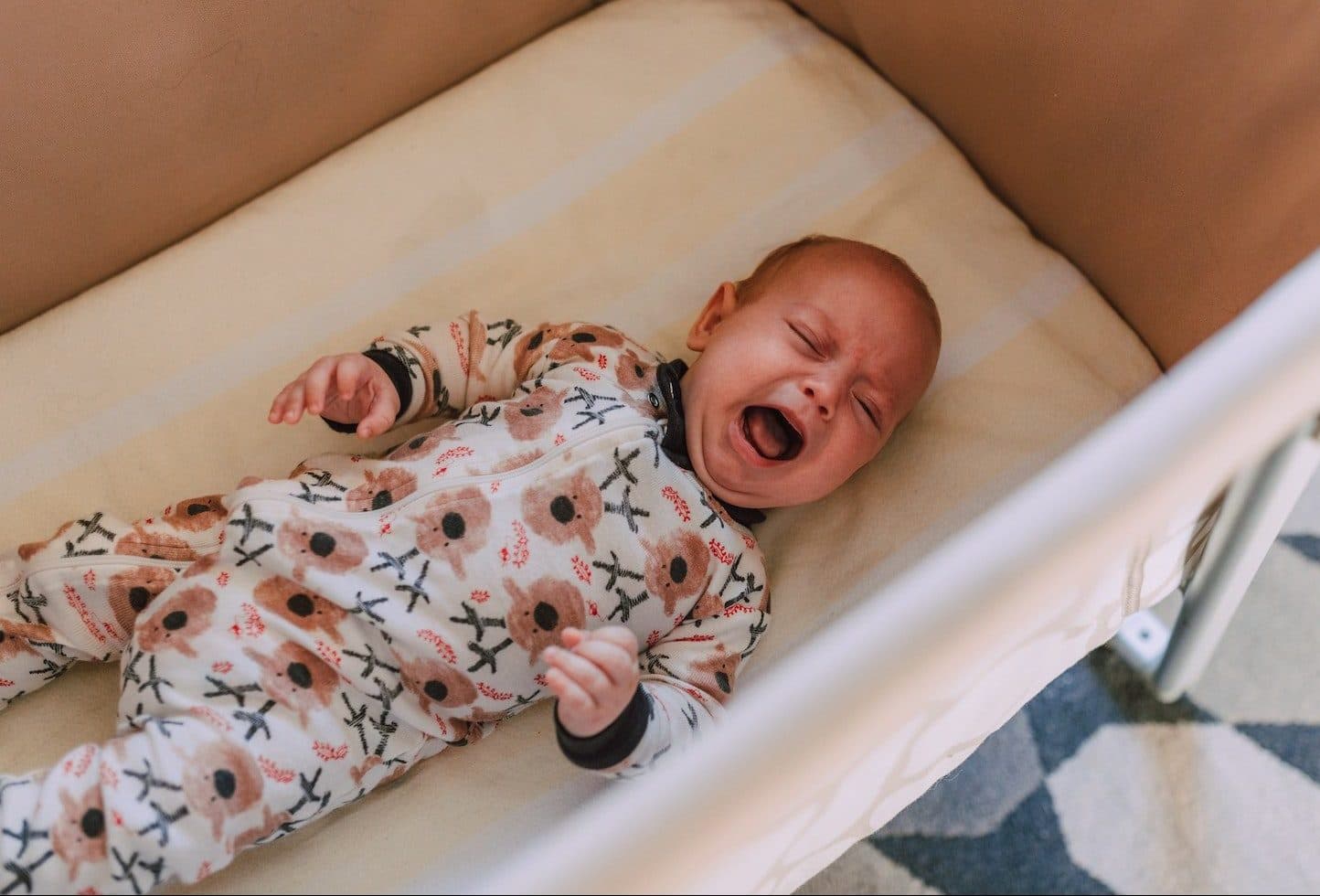 A Baby in Onesie Crying while Lying Down on Crib