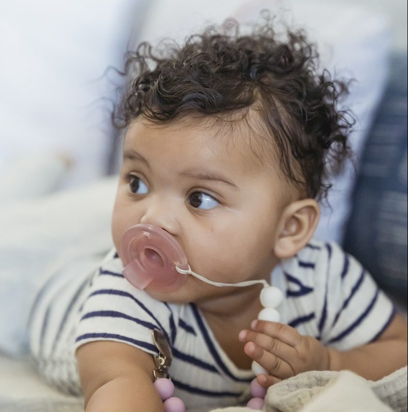 Adorable African American baby with curly hair looking away while lying on soft blanket on couch on blurred background at home