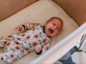 A Baby in Onesie Crying while Lying Down on Crib