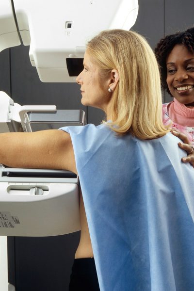 smiling woman standing near another woman beside mammogram machine