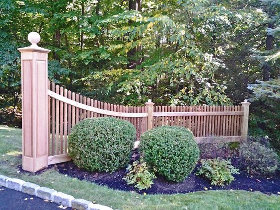 Sloped Wooden Fence With Large End Pole, Flowerbed With Shrubs And Colored Pebles