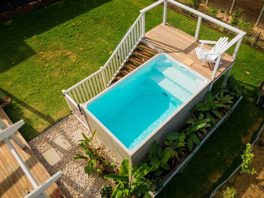 Above-ground Pool Witg Stairs And Small Seating Deck Surrounded By Gravel Flower Beds And Plants