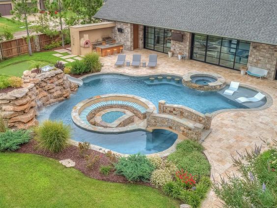 Lazy River Pool With Bridge Leading To Inground Seating Area And Waterfal Feature