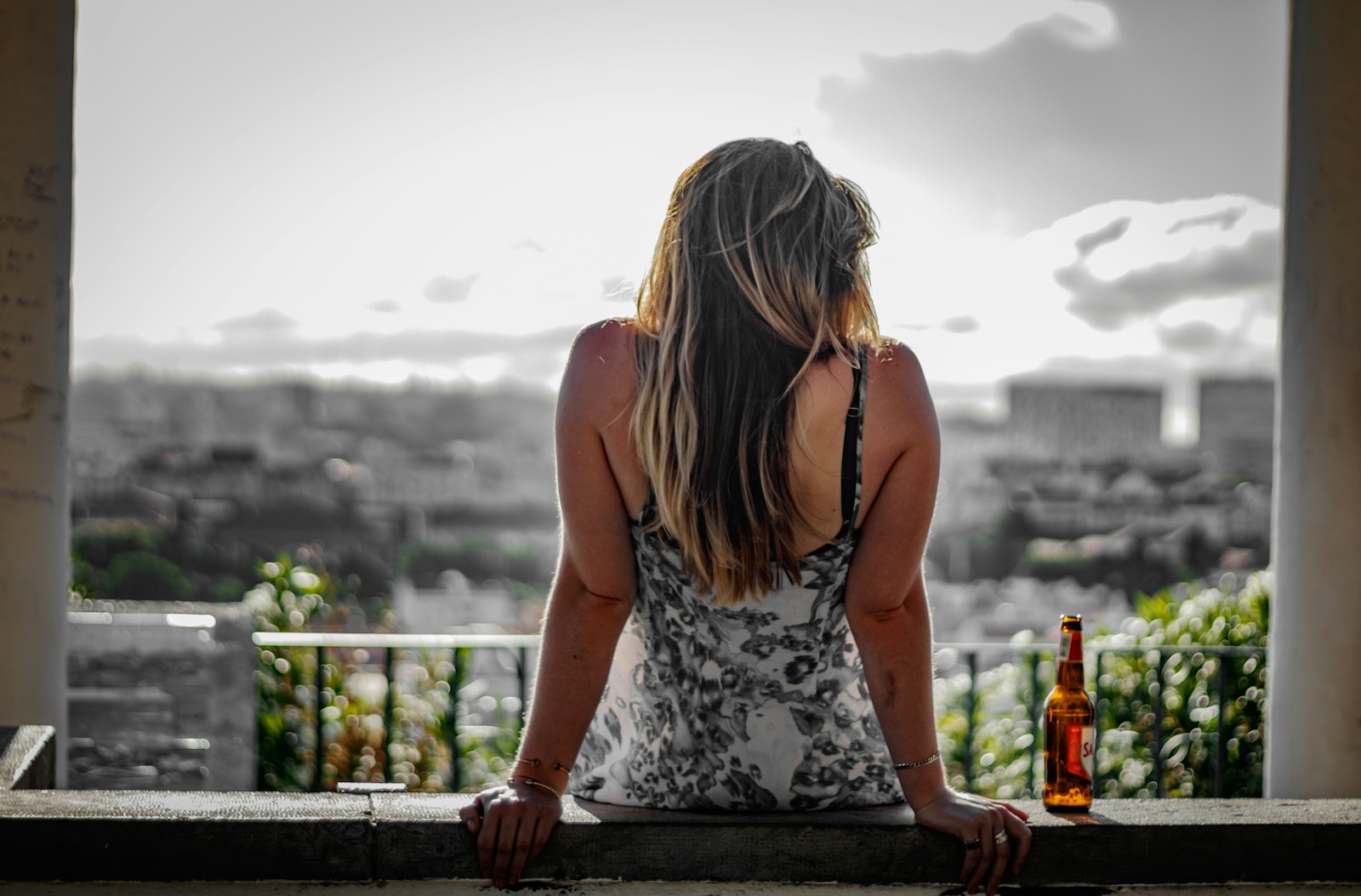 a woman sitting on a ledge with a bottle of beer